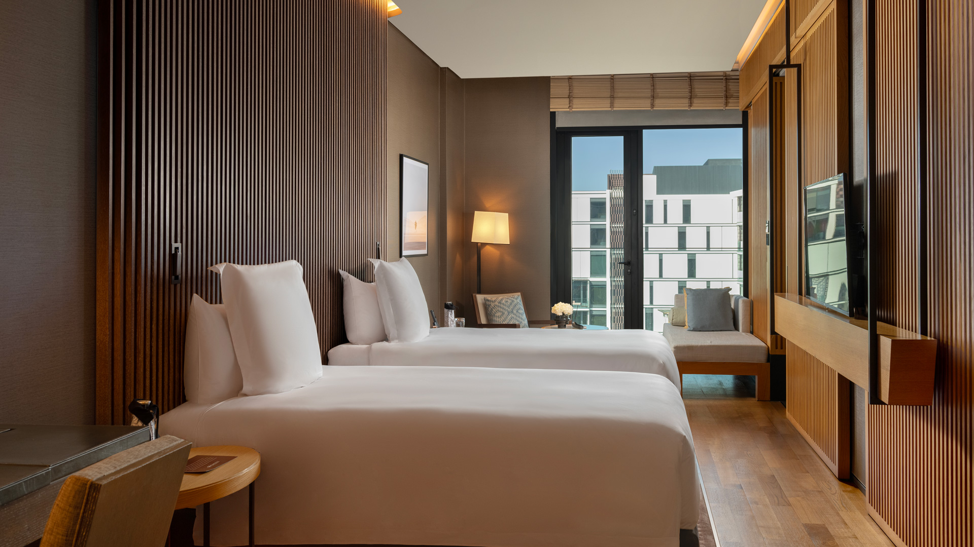 Twin beds in Banyan Tree Dubai bliss resort view guestroom, wood decor, window view of urban buildings.